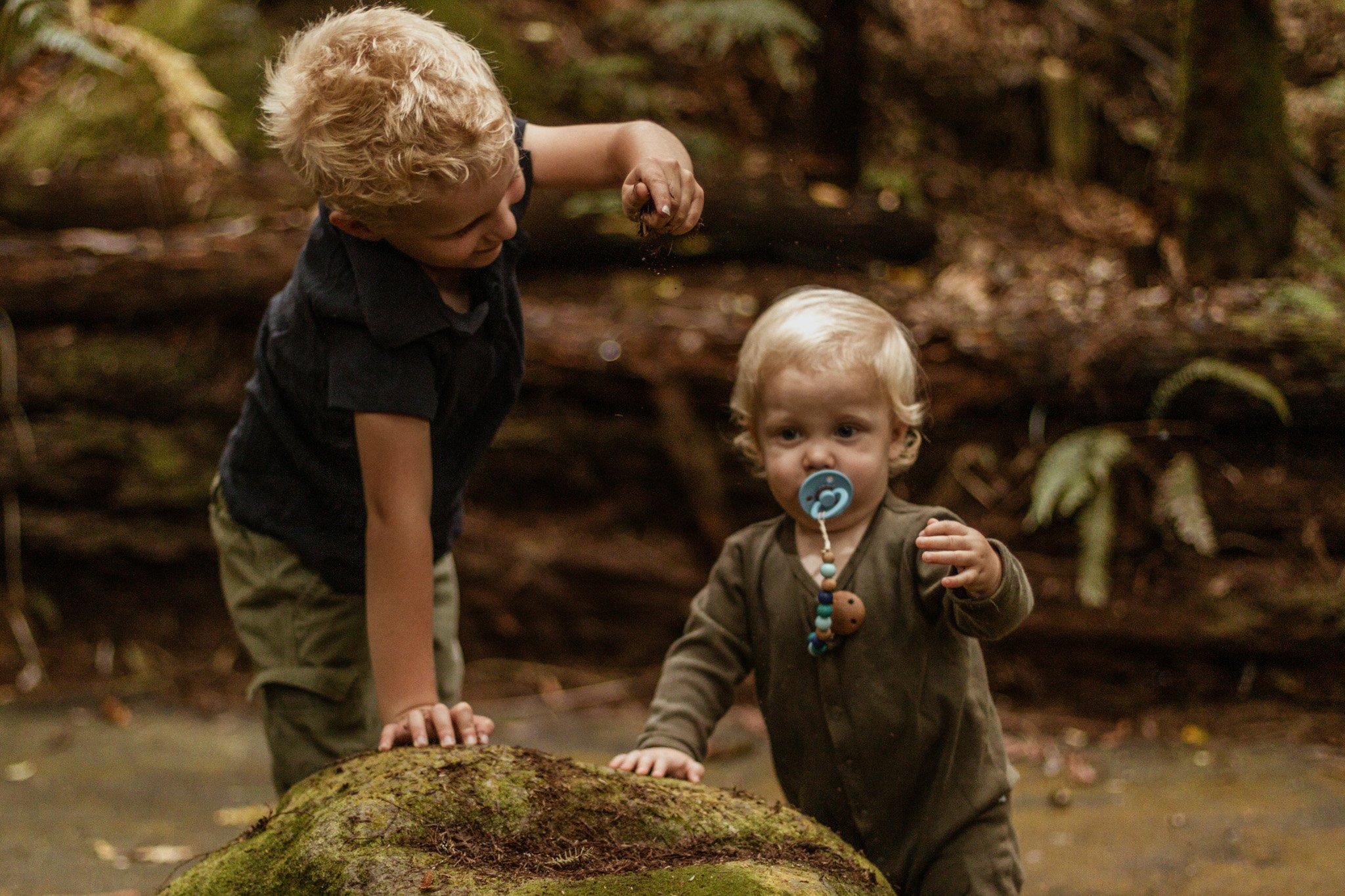 Two young boys playing outside leaning on a rock