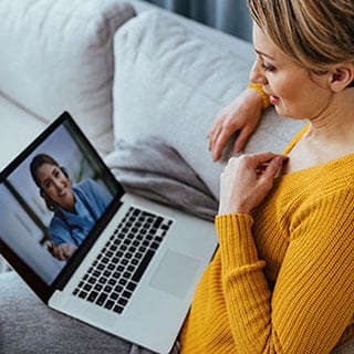 Woman using laptop and having video call with her doctor while sitting at home.