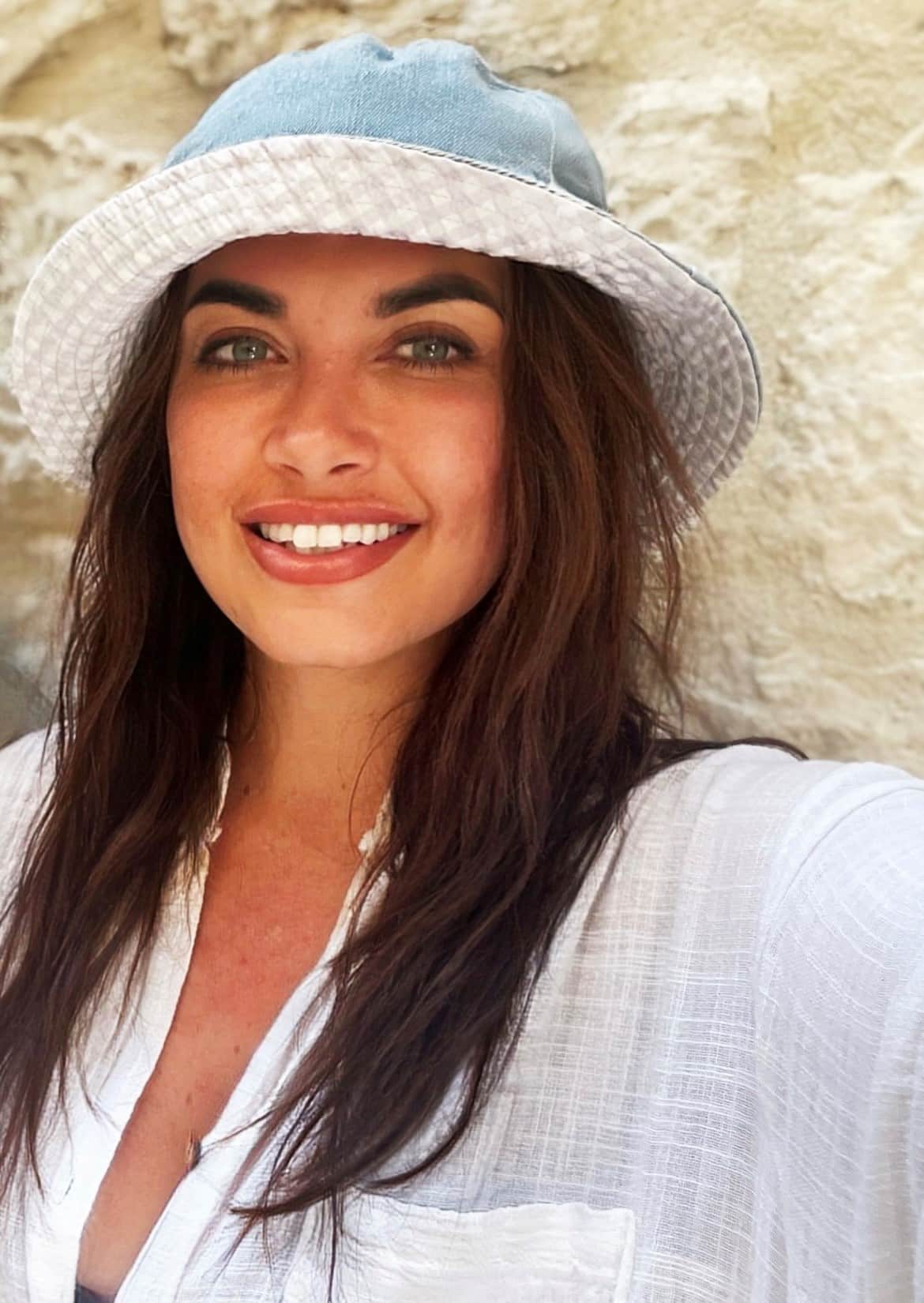Kiera wears a white top and white and blue hat and smiles at the camera.