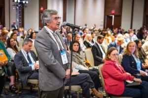 An attendee of a NORD event standing at a microphone to ask a presenter on stage a question