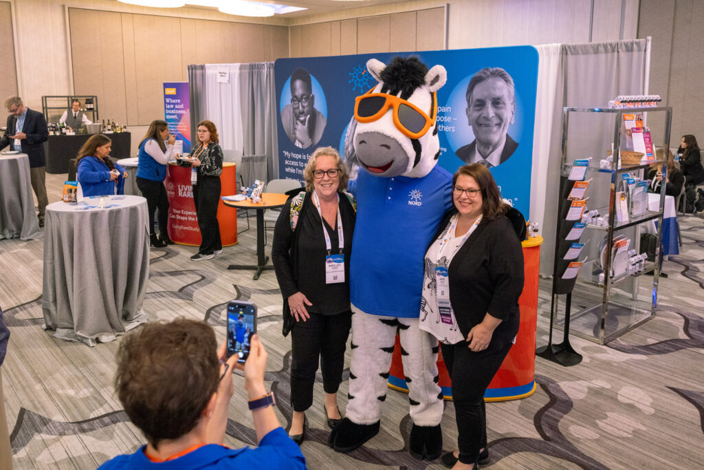 Two attendees posing with NORDY the zebra at the NORD Breakthrough Summit