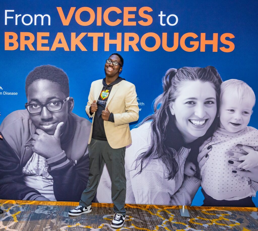 Micah Clayborne standing in front of an event sign on which he appears. The sign says, "From voices to breakthroughs.